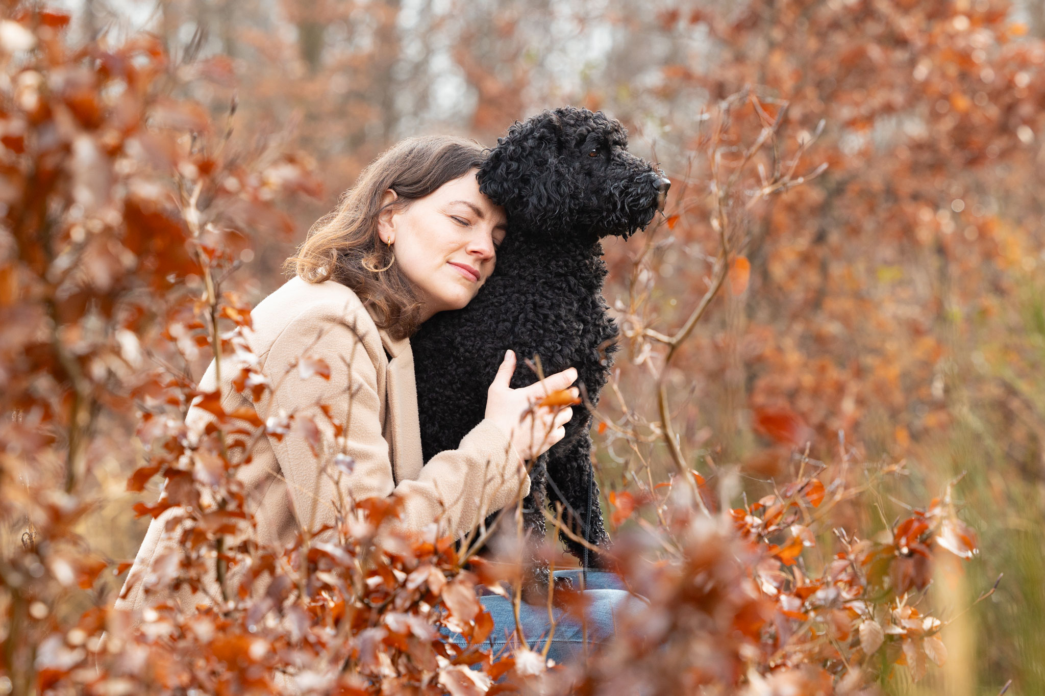 Frauchen sitzt mit ihrem Hund auf dem Schoß im Wald und lehnt sich vertraut an ihn.